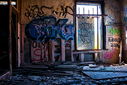 abandoned room with graffiti on walls and bars on window